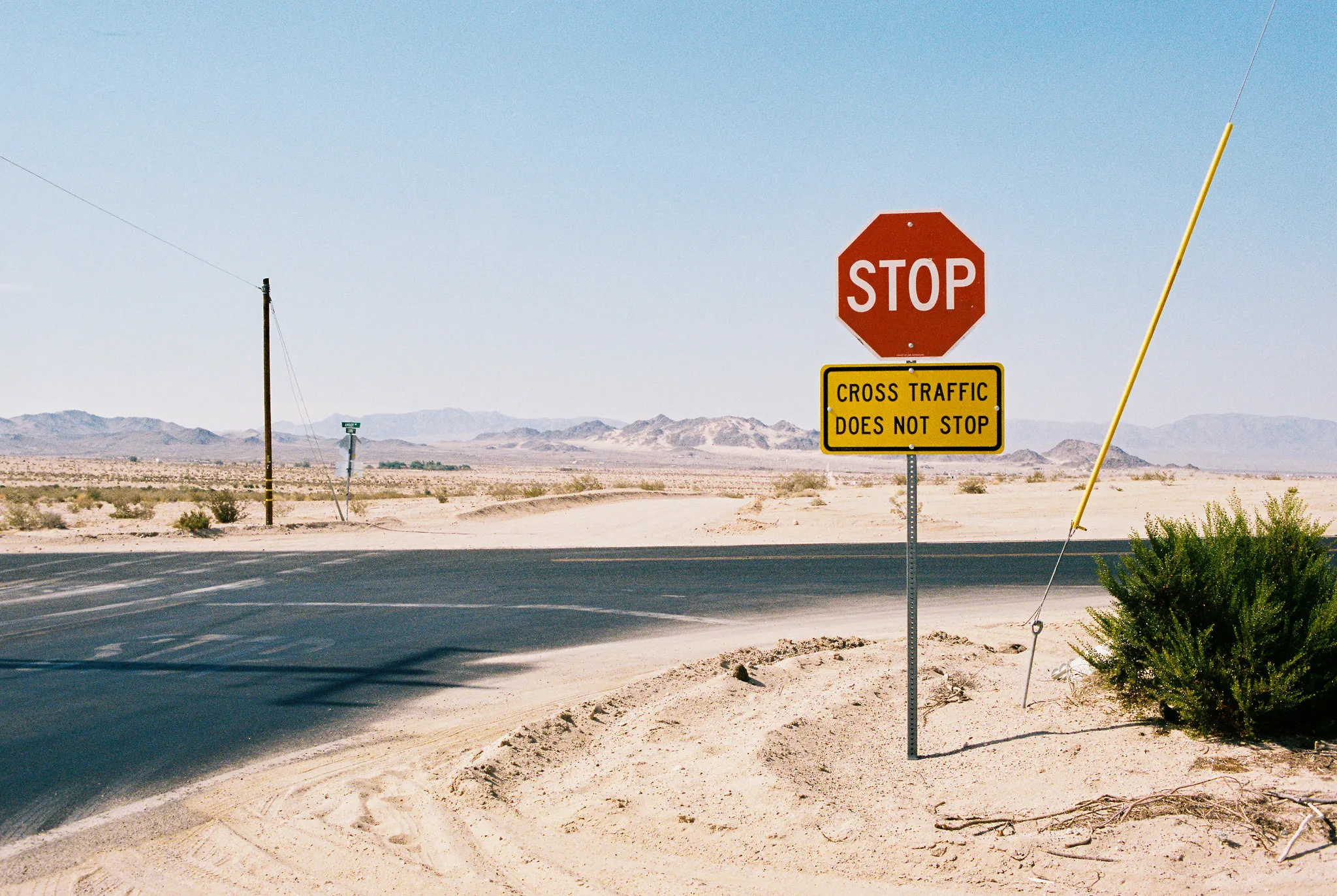 Stop sign with cross traffic warning on a sandy desert highway