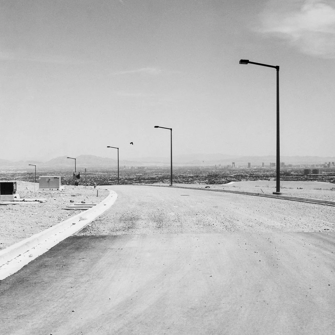 Black and white photograph of an unfinished Las Vegas subdivision with empty roads, streetlights, and the Strip dissolving into haze