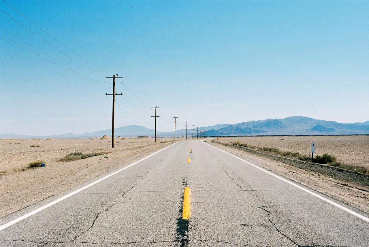 Two-lane highway vanishing into distant mountains with power lines in the Mojave Desert